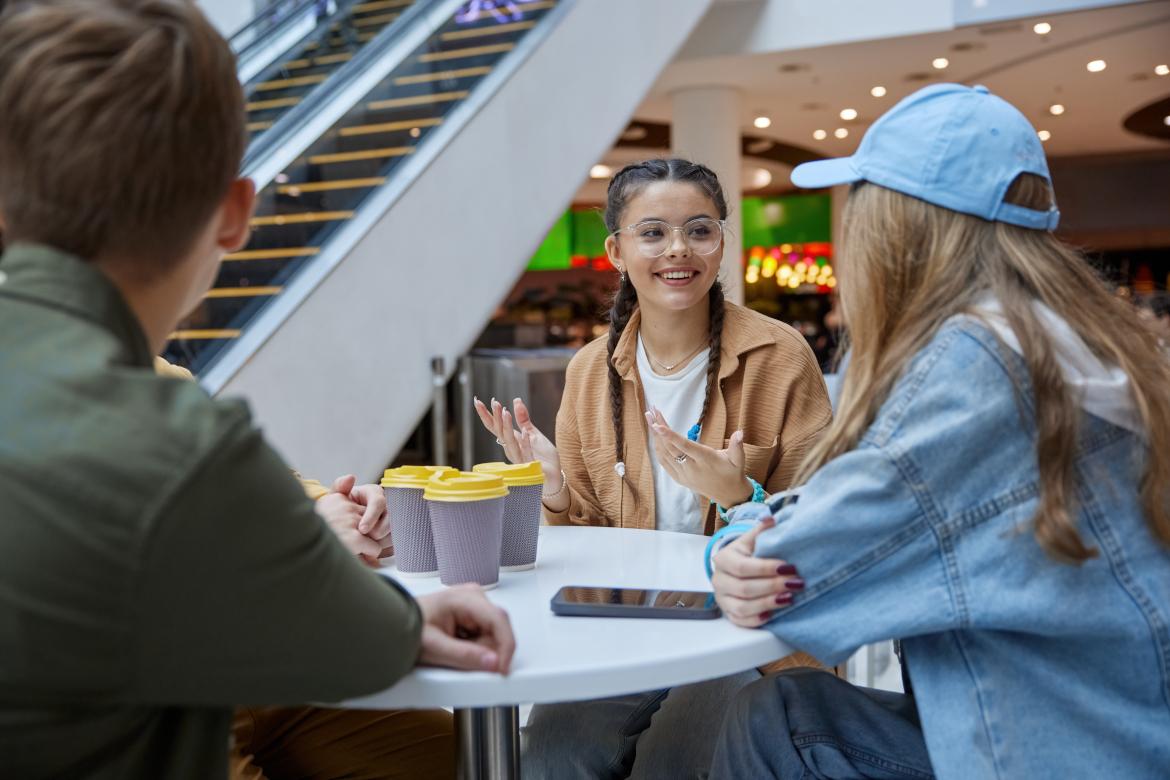 Jugendliche sitzen in Einkaufszentrum mit Kaffeebechern