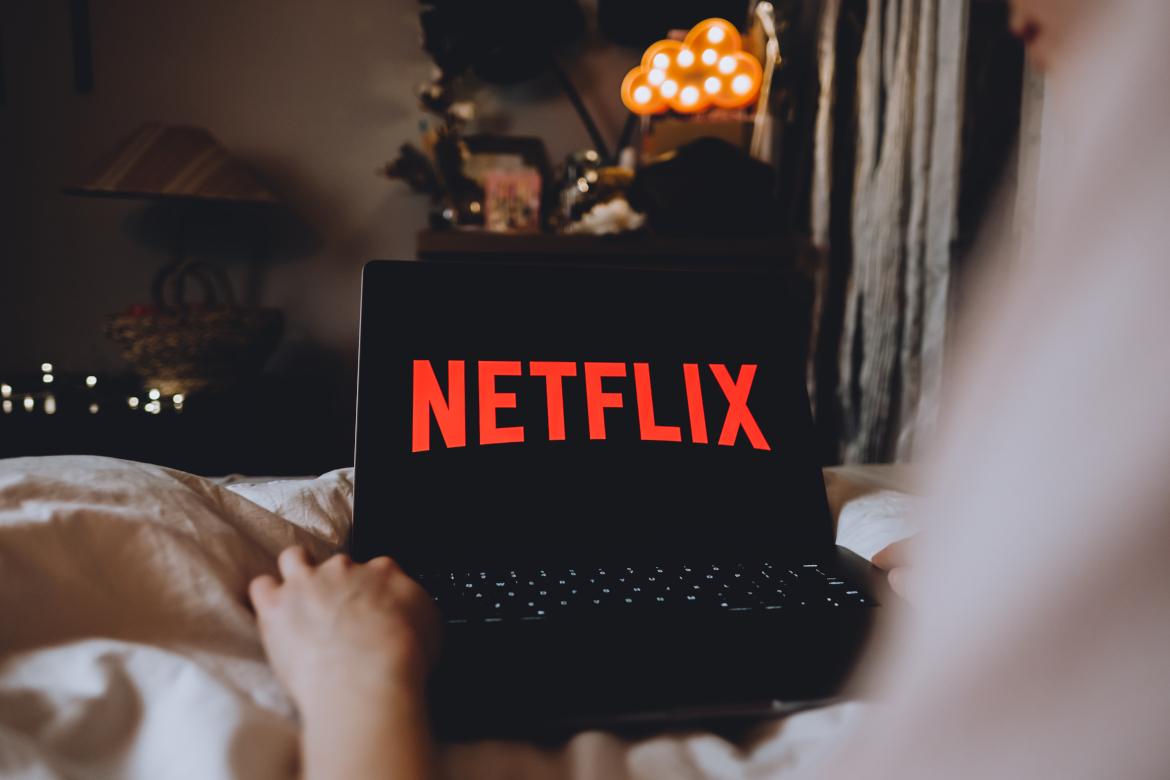 Person sitzt auf Sofa mit Laptop. Auf Bildschirm steht Netflix