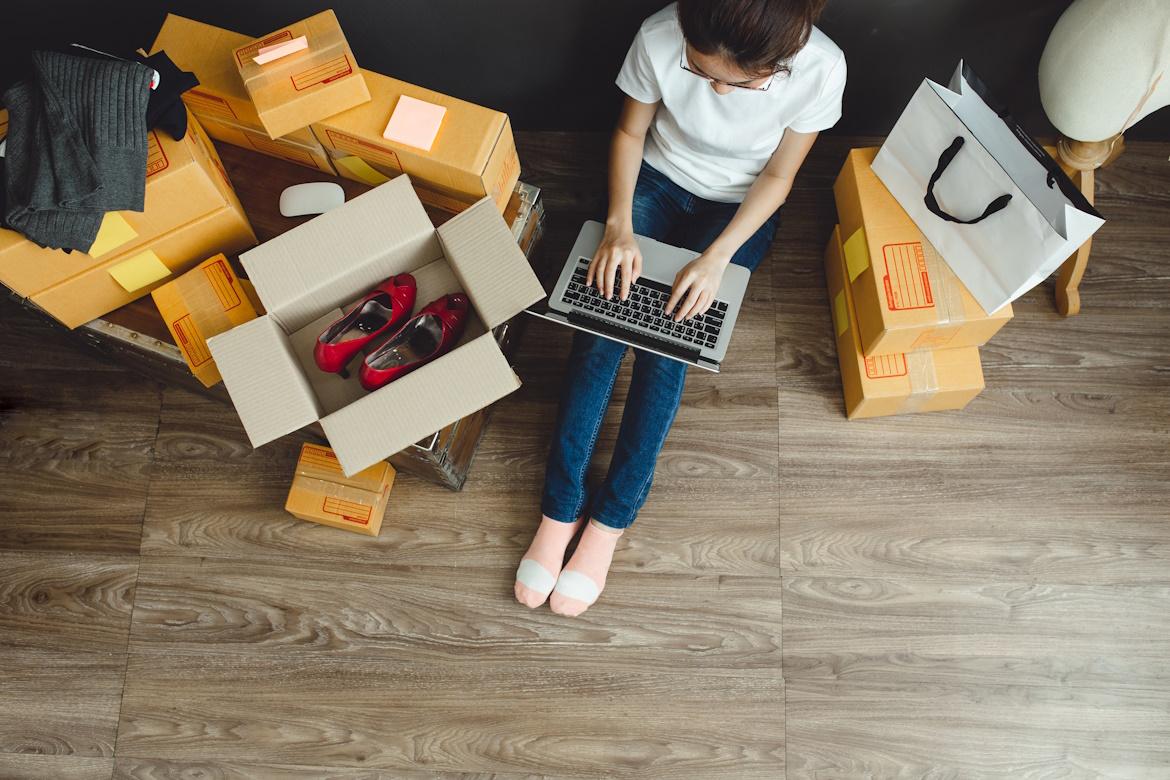 Frau mit Laptop und Kartons mit bestellten Produkten auf Boden China Shops