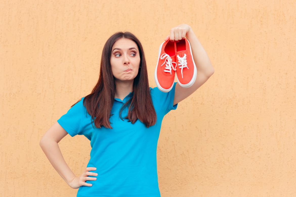 Frau hält  rote Turnschuhe in der Hand und macht ein kritisches Gesicht