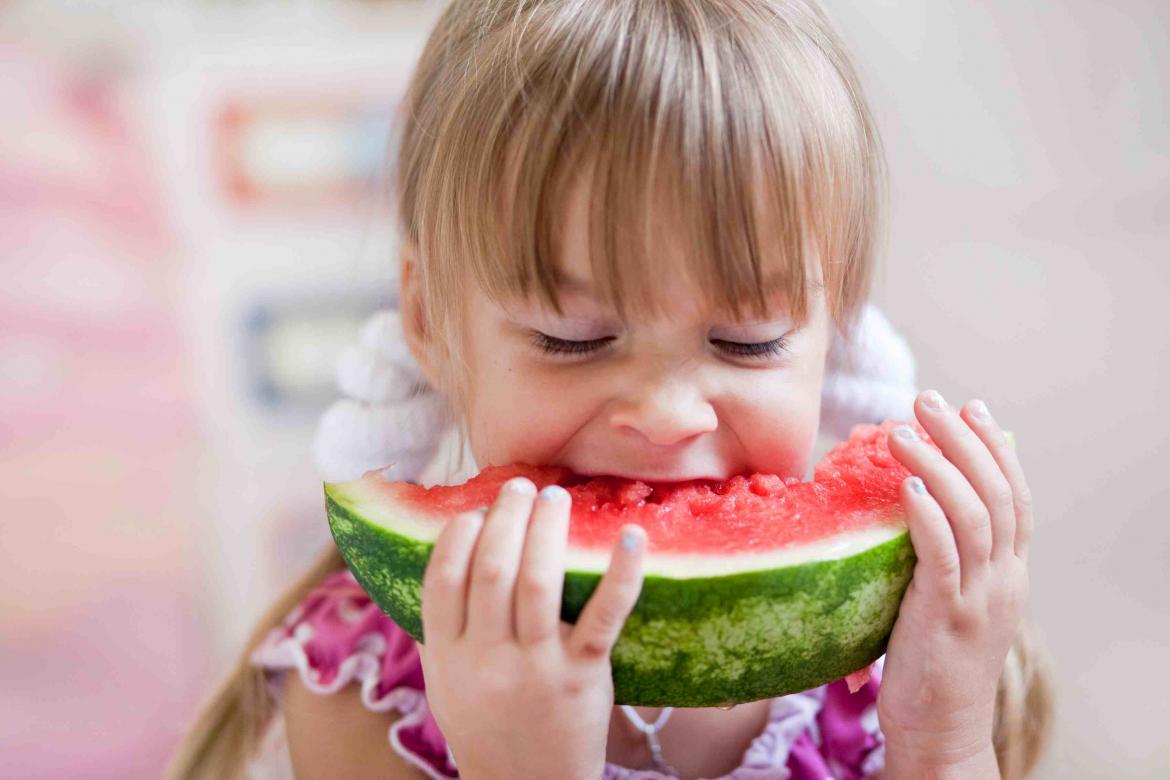 Mädchen beißt voller Genuß in ein Stück Wassermelone