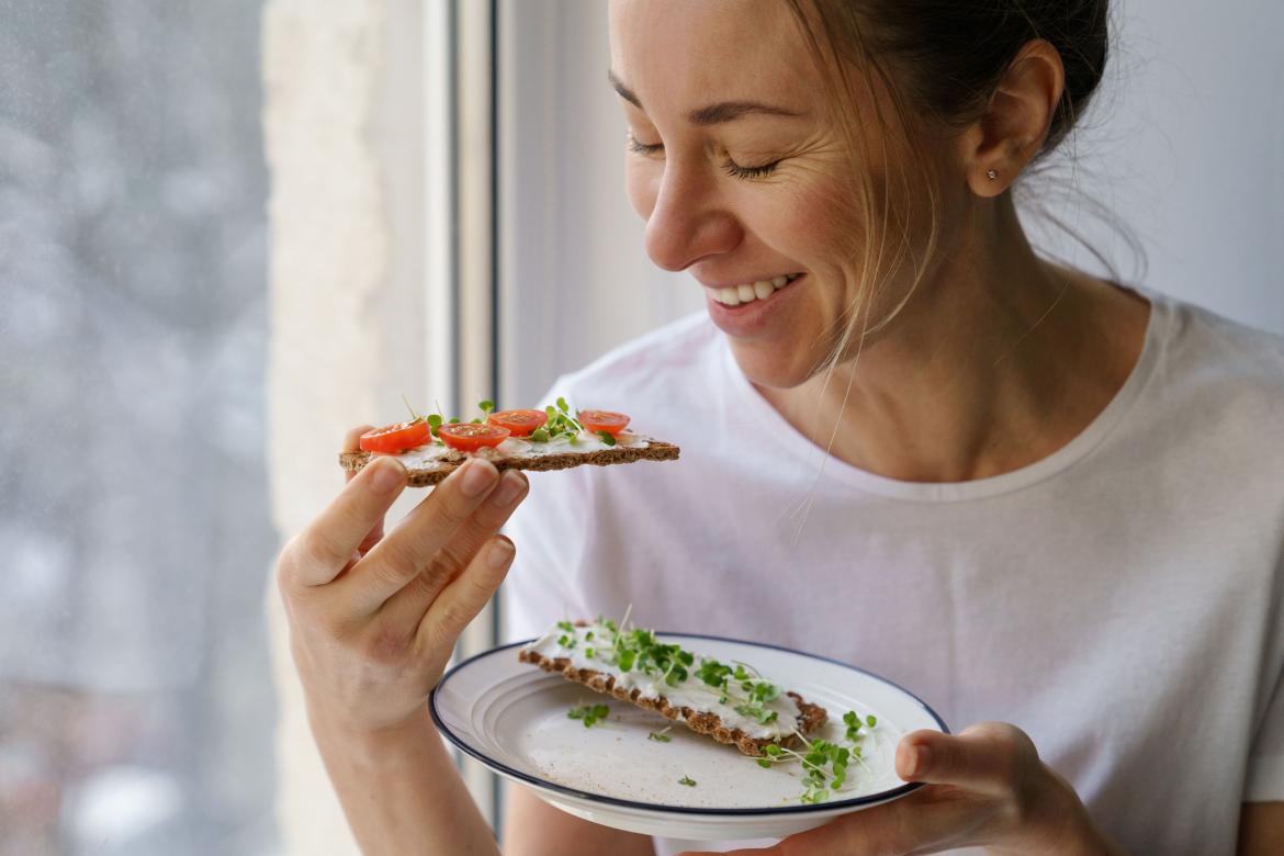 Frau hat eine belegtes Brot in der Hand und lächelt
