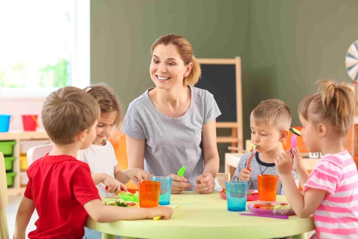 Erzieherrin sitzt mit Kindern am Tisch