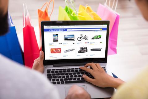 Bunte Tüten im Hintergrund, Computer mit geöffnetem Onlineshop zu Artikel: Amazon sperrt Kundenkonto nach zu vielen Retouren