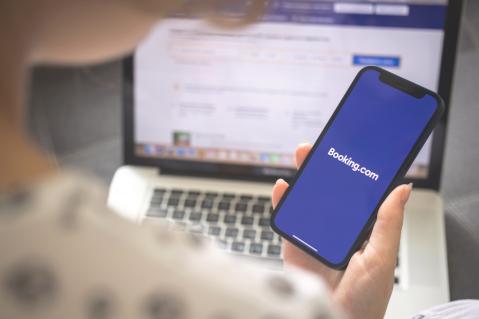 Frau mit Smartphone öffnet booking App, im Hintergrund Laptop