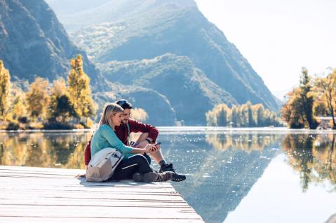 Pärchen auf Steg, See und Bergpanorama im Hintergrund zu Artikel: Grenznaher Urlaub: Wenn das Handy sich ins falsche Netz einwählt