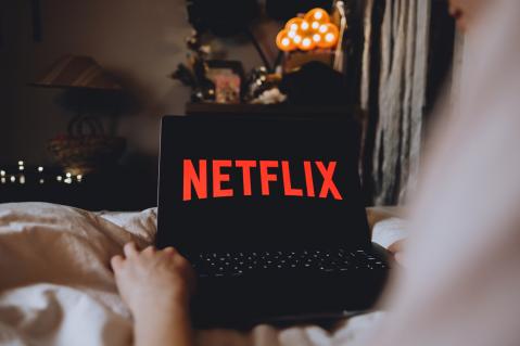 Person sitzt auf Sofa mit Laptop. Auf Bildschirm steht Netflix
