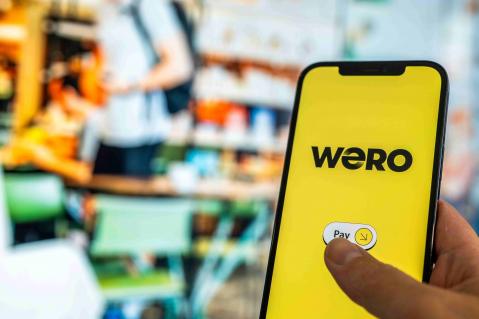 Wero Pay App auf Handy im Vordergrund - Hintergrund Supermarktregale verschwommen
