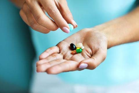 Hand auf türkisem Hintergrund mit Pillen und Tabletten