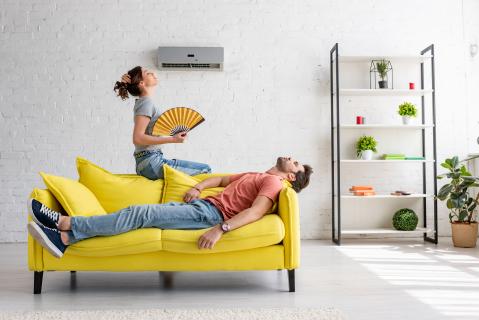 Gelbe Couch: Er liegt auf der couch - ihm ist sichtlich zu warm. Sie sitz auf der Rückenlehne der Couch und hat einen Fächer in der Hand.