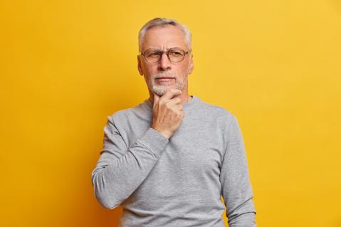 Ältererer Mann auf gelbem Hintergrund hat Hand am Kinn und schaut nachdenklich