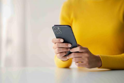 Frau mit gelbem Oberteil hat Handy in der Hand