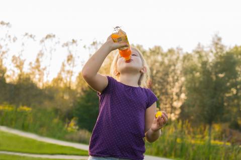 Kind trinkt draußen ein Kindergetränk, ähnlich Multivitaminsaft aus einer Flasche