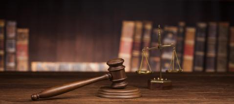 Hammer auf Unterlage mit Gesetzesbüchern im Hintergrund