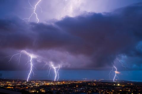 Auf dem Foto sind mehre Blitze zu sehen, am unteren Bildrand Häuser. Der Himmel ist dunkel.