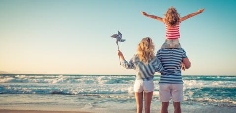Familie am Strand von hinten, Kind auf Schultern des Vaters. Es ist Sommer.